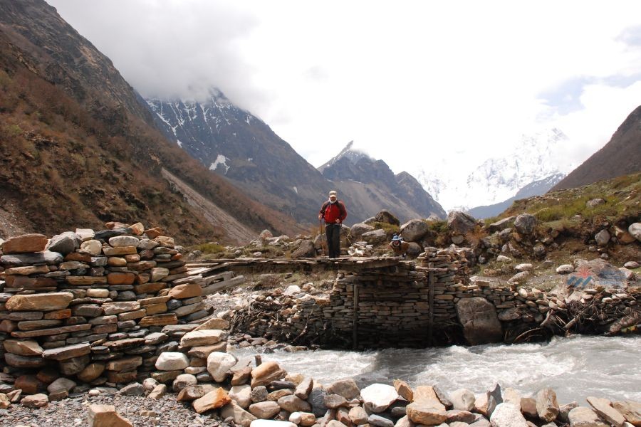 Trekker crossing a stone bridge over a mountain river.